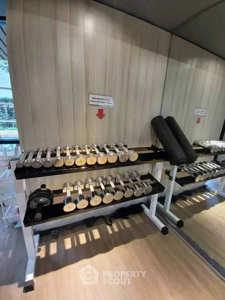 Modern gym with sleek dumbbell rack and mirrored wall in luxury apartment complex.