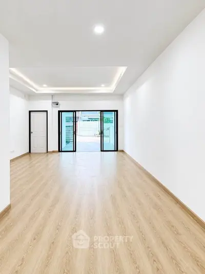 Spacious modern living room with wooden flooring and large glass doors leading to a balcony.