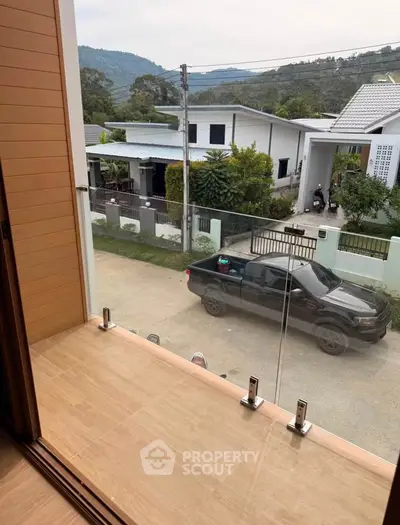Modern balcony view with glass railing overlooking residential street and mountain backdrop.