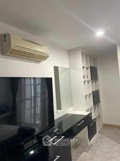 Modern living room with sleek black furniture and built-in shelving, featuring a wall-mounted air conditioner.