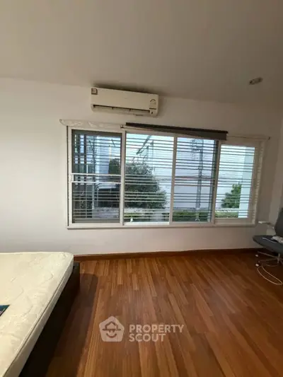 Spacious bedroom with large window and wooden flooring, featuring air conditioning for comfort.