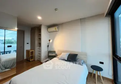 Modern bedroom with wooden flooring and large window offering city view.