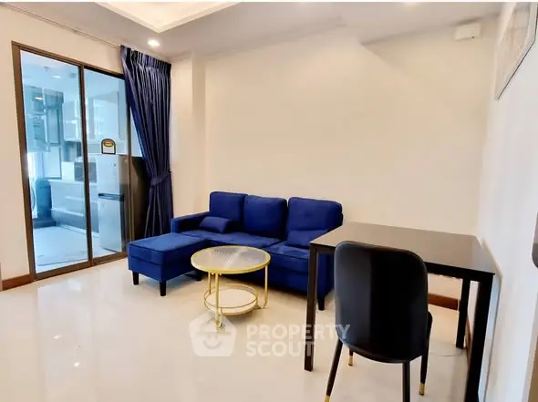 Modern living room with blue sofa, glass door, and sleek furniture in a stylish apartment.