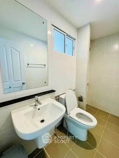 Modern bathroom with sleek fixtures and neutral tiles, featuring a large mirror and natural light.