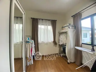 Cozy bedroom with wooden flooring and ample natural light, featuring a mirrored wardrobe and organized clothing rack.