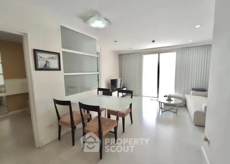 Modern living room with dining area and natural light, featuring sleek furniture and minimalist design.