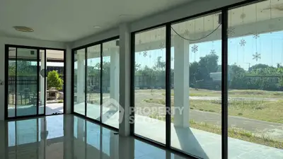 Spacious modern living room with large glass windows offering abundant natural light and garden view.