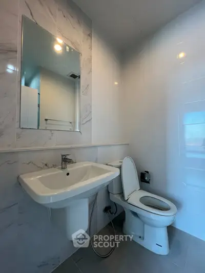 Modern bathroom with sleek fixtures and marble tiles, featuring a wall-mounted sink and toilet.