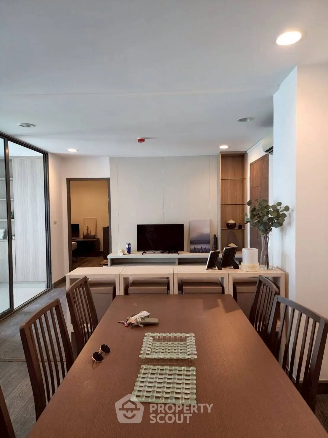 Modern dining area with sleek wooden table and chairs, adjacent to a cozy living room with TV and decor.