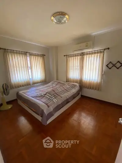 Cozy bedroom with wooden flooring and natural light from large windows