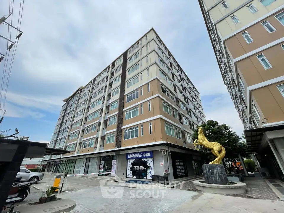 Modern multi-story apartment building with commercial spaces and unique sculpture in urban setting.