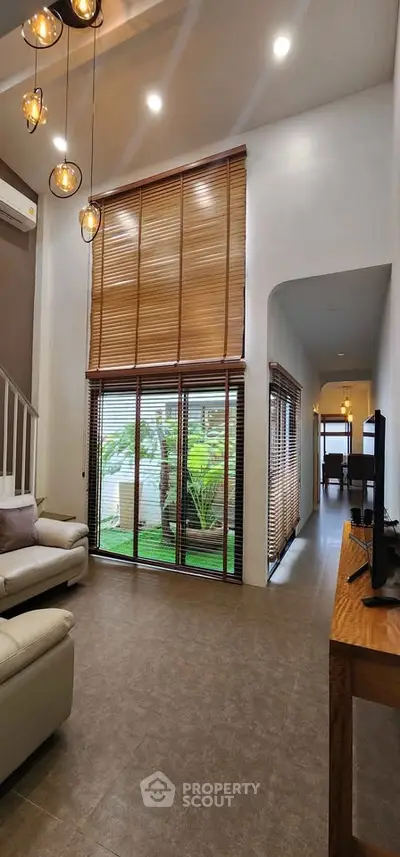 Spacious living room with high ceilings, modern lighting, and large windows overlooking a lush garden.