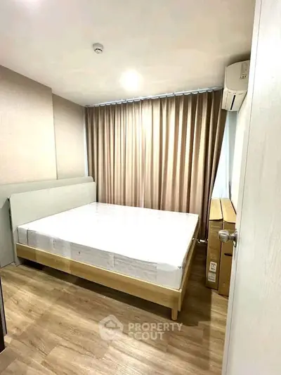 Modern bedroom with wooden flooring and natural light, featuring a comfortable bed and air conditioning.