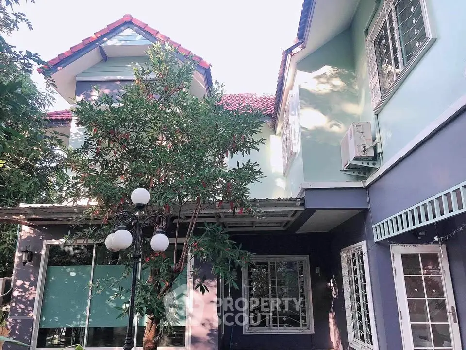 Charming two-story house with red roof and lush greenery, perfect for family living.