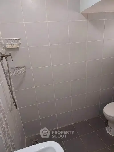 Minimalist bathroom with tiled walls and shower area, featuring a simple design.