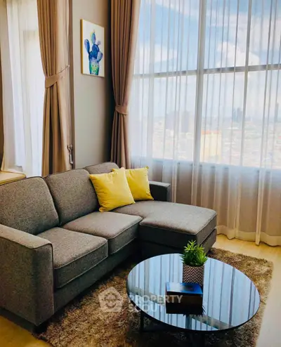 Stylish living room with large windows and modern gray sofa in high-rise apartment.
