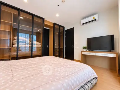Modern bedroom with glass wardrobe and TV, featuring cozy bedding and air conditioning.