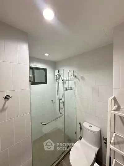 Modern bathroom with glass shower enclosure and sleek white tiles.