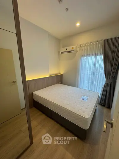 Modern bedroom with large window and air conditioning, featuring a comfortable mattress and wooden flooring.