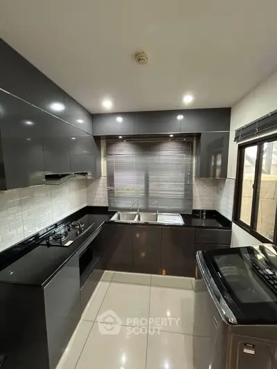 Modern kitchen with sleek black cabinetry and gas stove, featuring a washing machine and ample natural light.