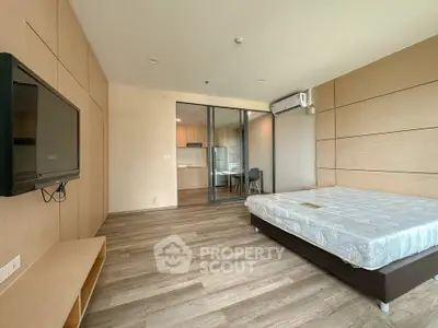 Spacious modern bedroom with wooden flooring and sliding glass doors leading to a kitchen area.