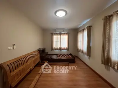 Spacious unfurnished bedroom with wooden flooring and ample natural light from large windows.
