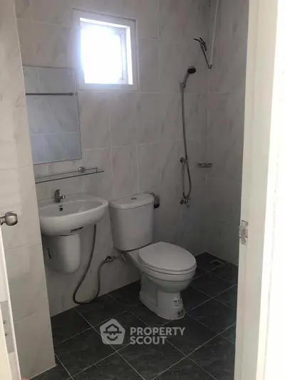Compact bathroom with modern fixtures and tiled walls, featuring a window for natural light.