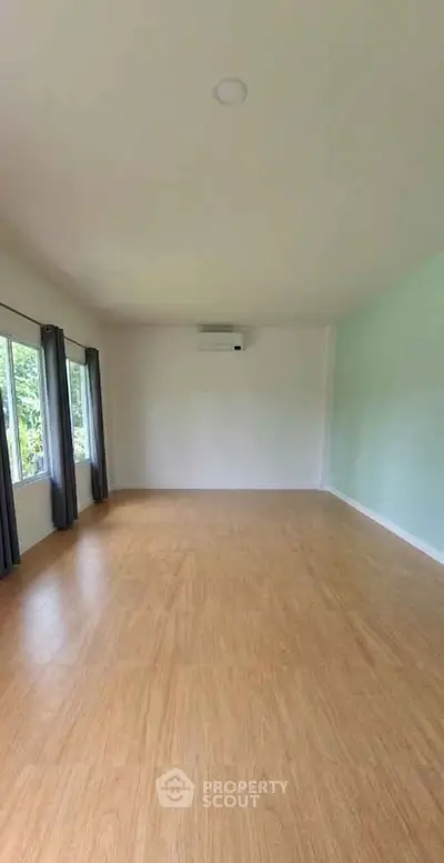 Spacious empty room with wooden flooring and large windows, perfect for customization.