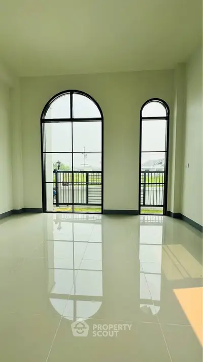 Spacious living room with large arched windows and glossy tiled floor, offering abundant natural light.