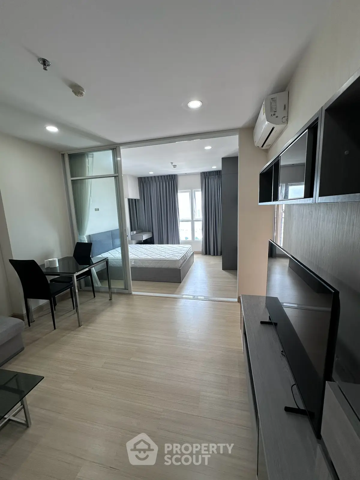Modern apartment interior with open layout, featuring a cozy living area and a bedroom with sliding glass doors.