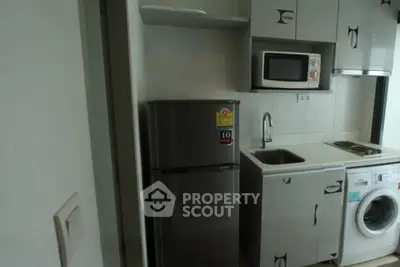 Compact kitchen with modern appliances including fridge, microwave, and washing machine in a cozy apartment.
