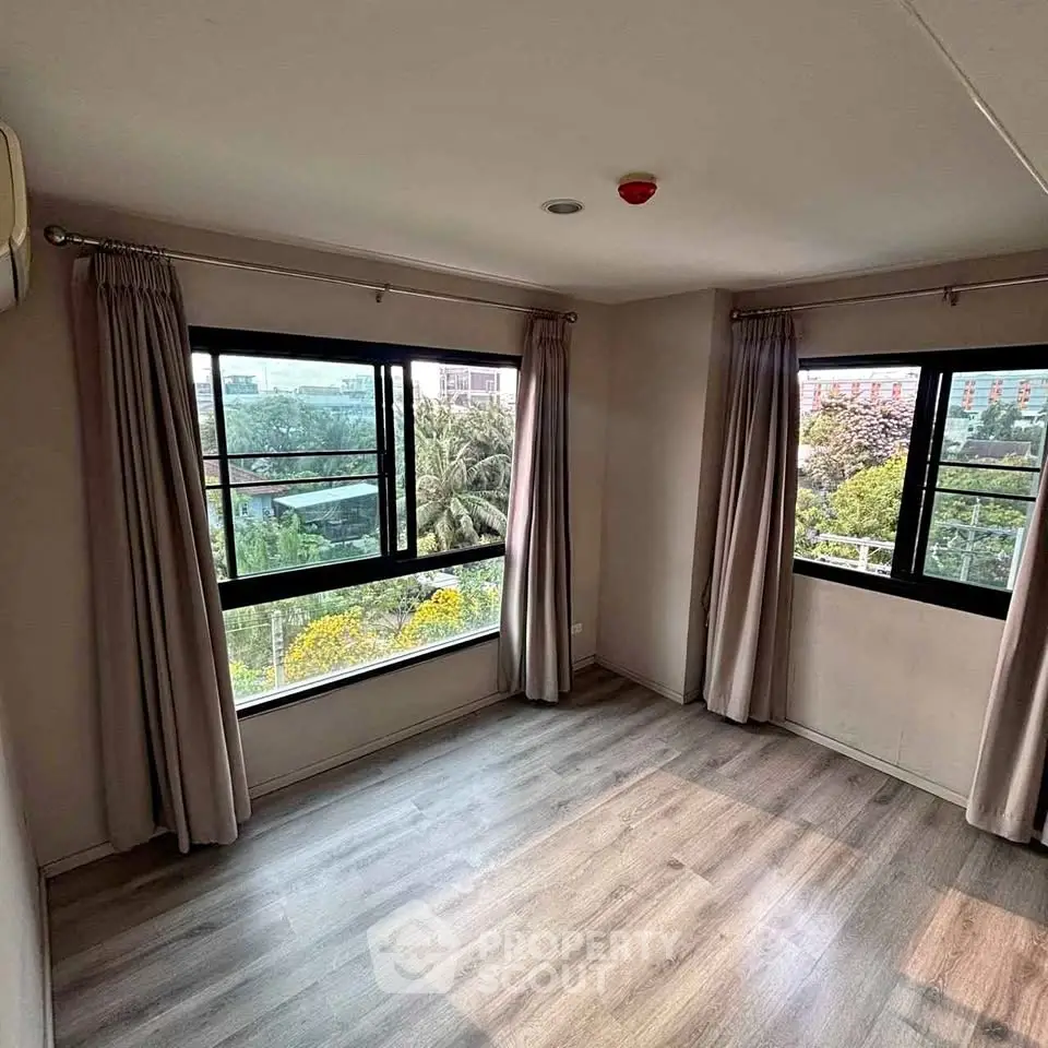 Bright empty room with large windows and wooden flooring, offering a serene garden view.