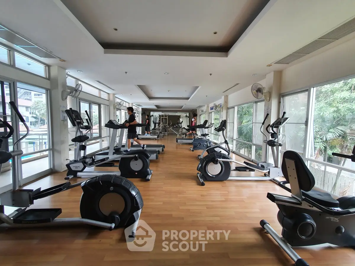 Spacious gym with modern equipment and large windows offering a lush garden view.