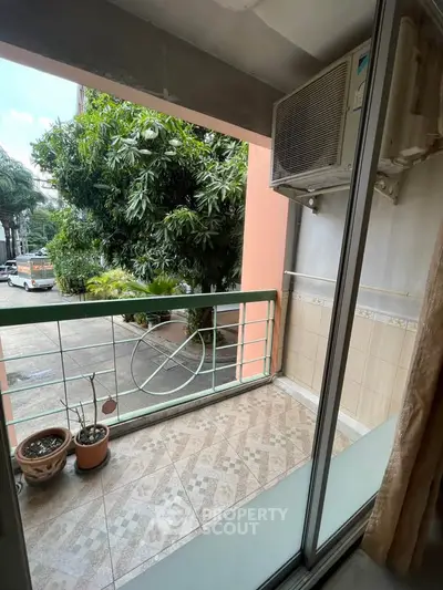 Charming balcony with lush greenery view and air conditioning unit, perfect for relaxation.