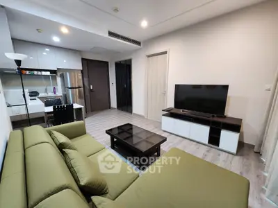 Modern living room with green sofa, sleek TV unit, and compact kitchen area in open layout apartment.