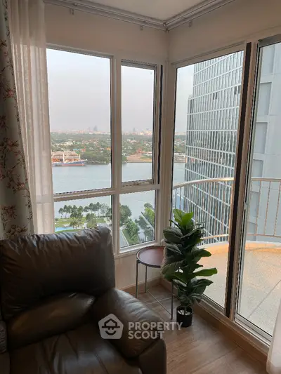 Luxurious corner unit with expansive windows offering a panoramic city and water view, complemented by a cozy seating area and natural light.