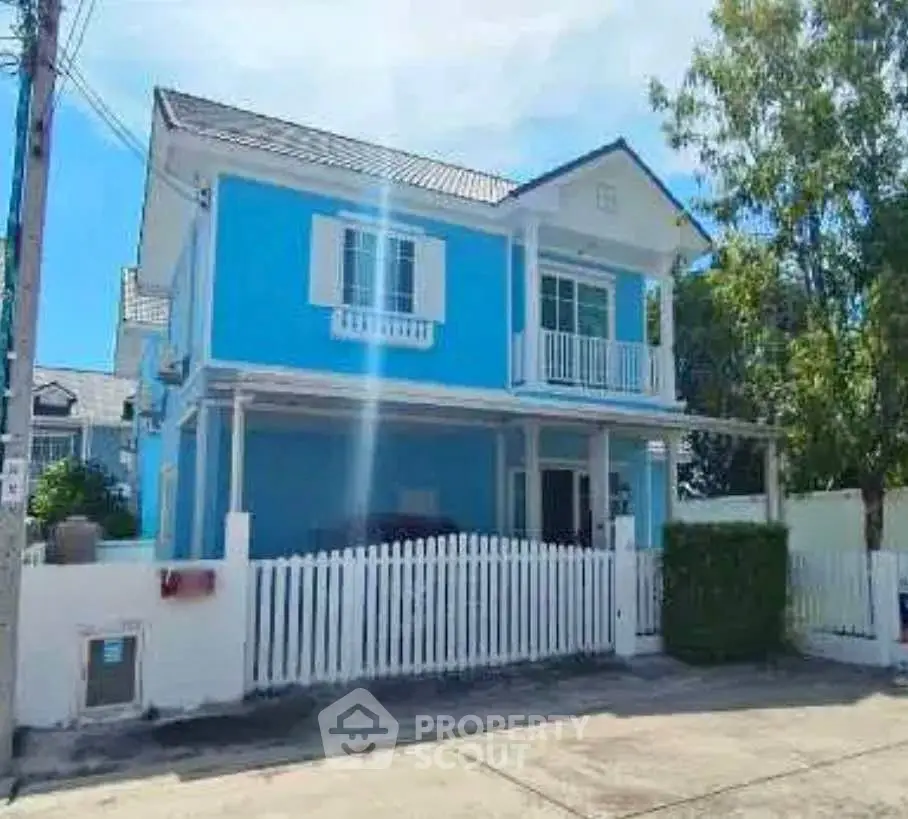 Charming blue two-story house with white picket fence and lush greenery