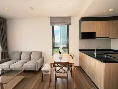 Modern living room with open kitchen and city view, featuring sleek wooden finishes and cozy seating area.