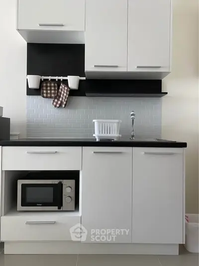 Modern kitchen with sleek white cabinets and built-in microwave, featuring a stylish backsplash.