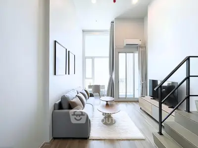 Modern living room with high ceilings, stylish furniture, and large windows leading to a balcony.
