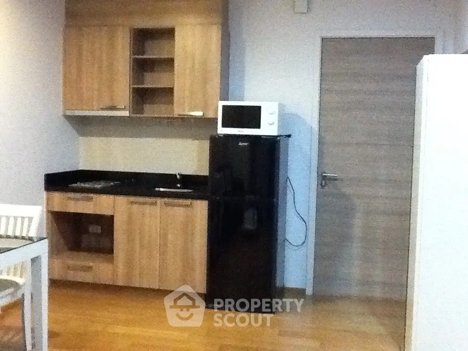 Modern kitchen with wooden cabinets, black fridge, and microwave in compact layout.