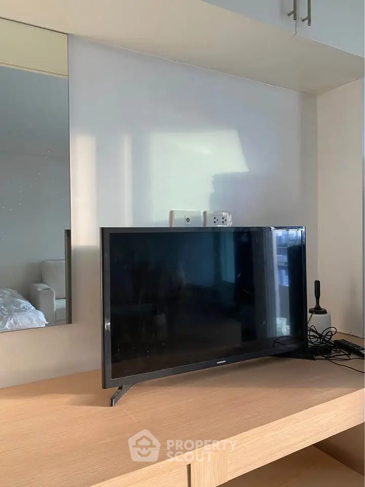 Modern bedroom with TV on wooden desk and mirror reflecting natural light