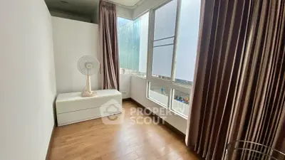 Bright room with large windows and wooden flooring, featuring a fan and curtains.