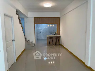 Modern open-plan living area with sleek staircase and breakfast bar in stylish home.