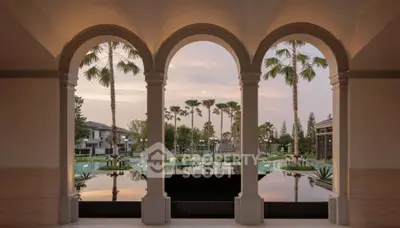 Luxurious resort-style view with elegant arches overlooking a serene pool and lush palm trees at sunset.