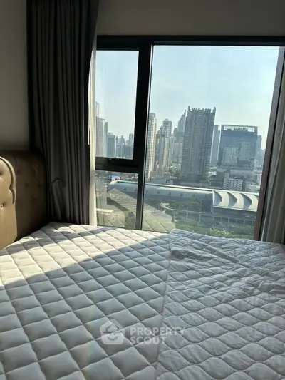 Modern bedroom with city view, featuring large window and stylish bedding.