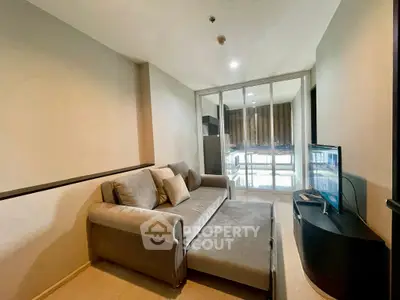 Cozy living room with modern sofa and TV, featuring glass doors leading to a bright balcony.