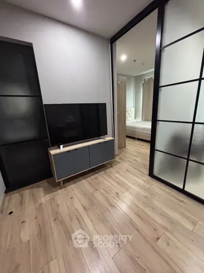 Modern apartment interior with sleek wooden flooring and stylish sliding doors leading to a cozy bedroom.