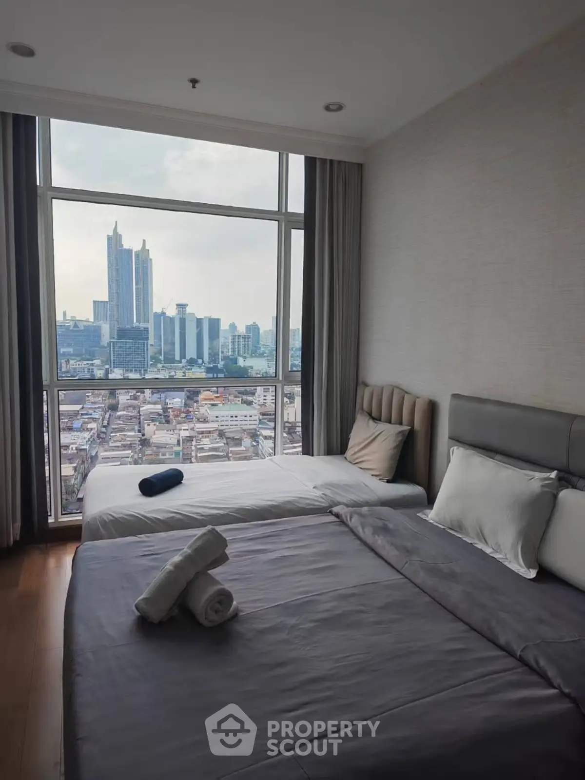 Modern bedroom with city view, featuring large windows and cozy bedding.