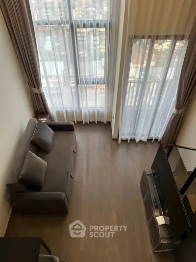 Modern living room with high ceilings and large windows offering city views.